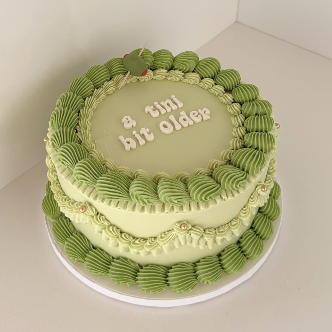 Olive martini themed cake with "a tini bit older" in block letters and a green olive