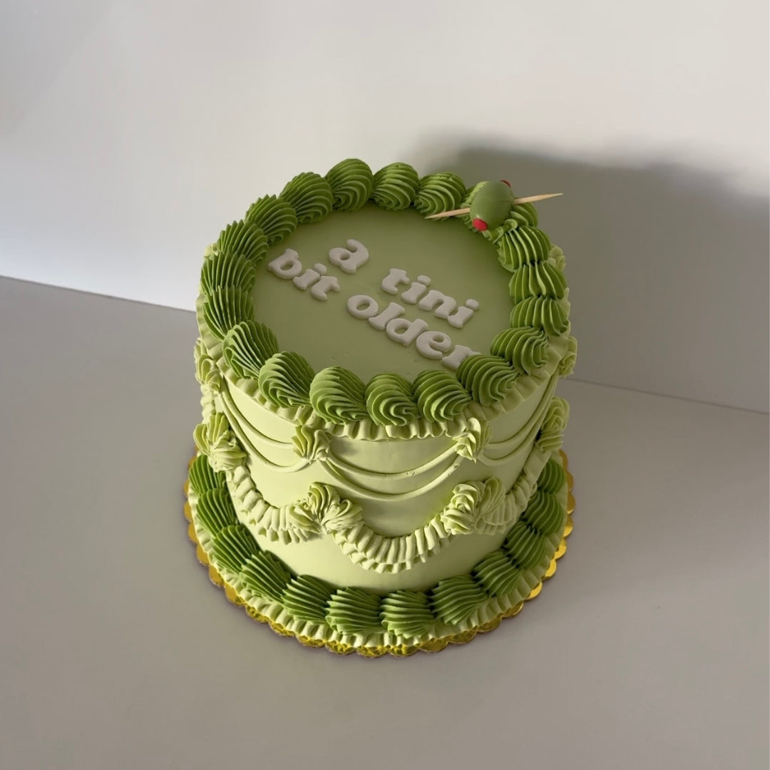 Olive martini themed cake with "a tini bit older" in block letters and a green olive