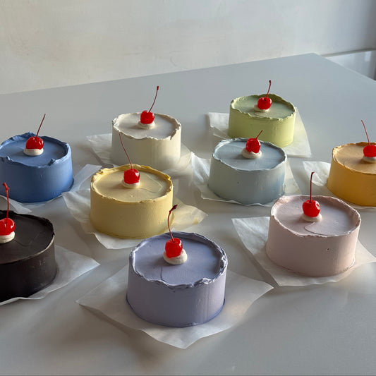 Nine small round cakes with cherry toppings on a white surface.