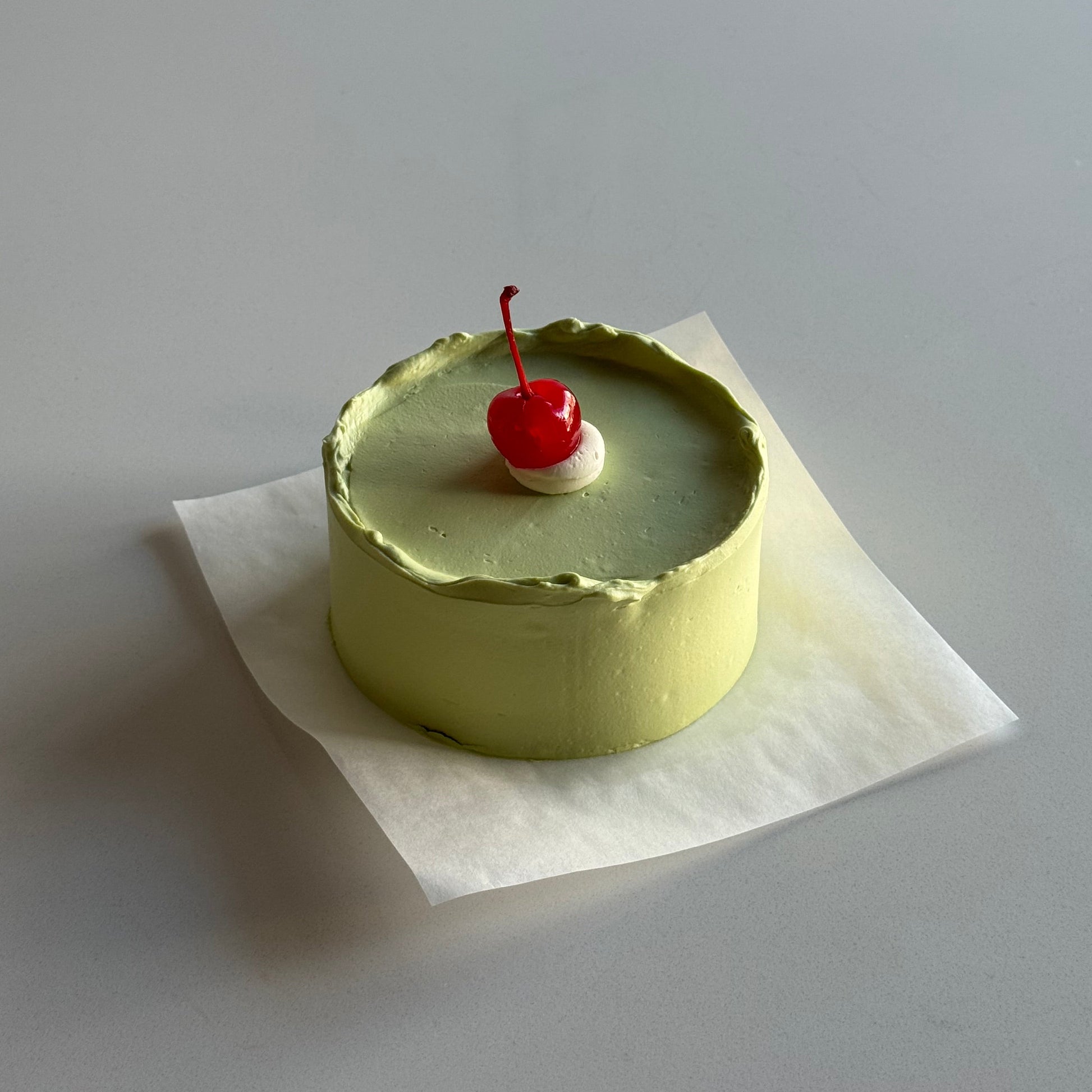 Small round cake with a red cherry on top, placed on a white surface.