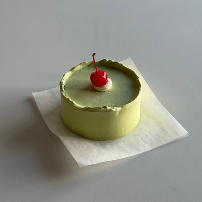 Small round cake with a red cherry on top, placed on a white surface.