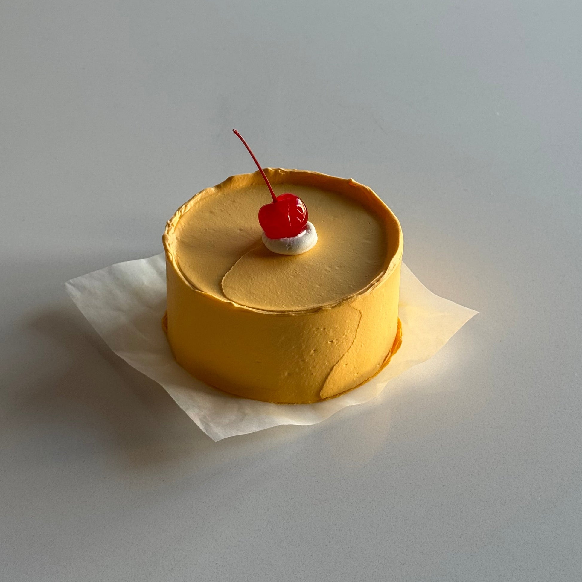 Yellow cake with a cherry on top attached to a white wall