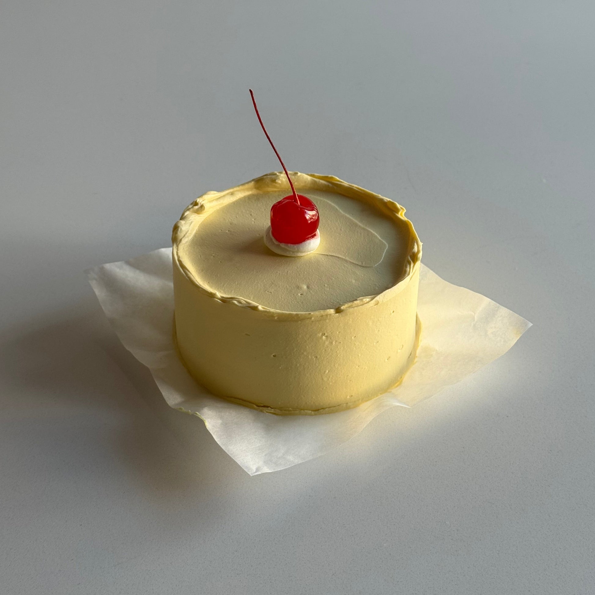 Small round cake with a cherry on top against a plain background