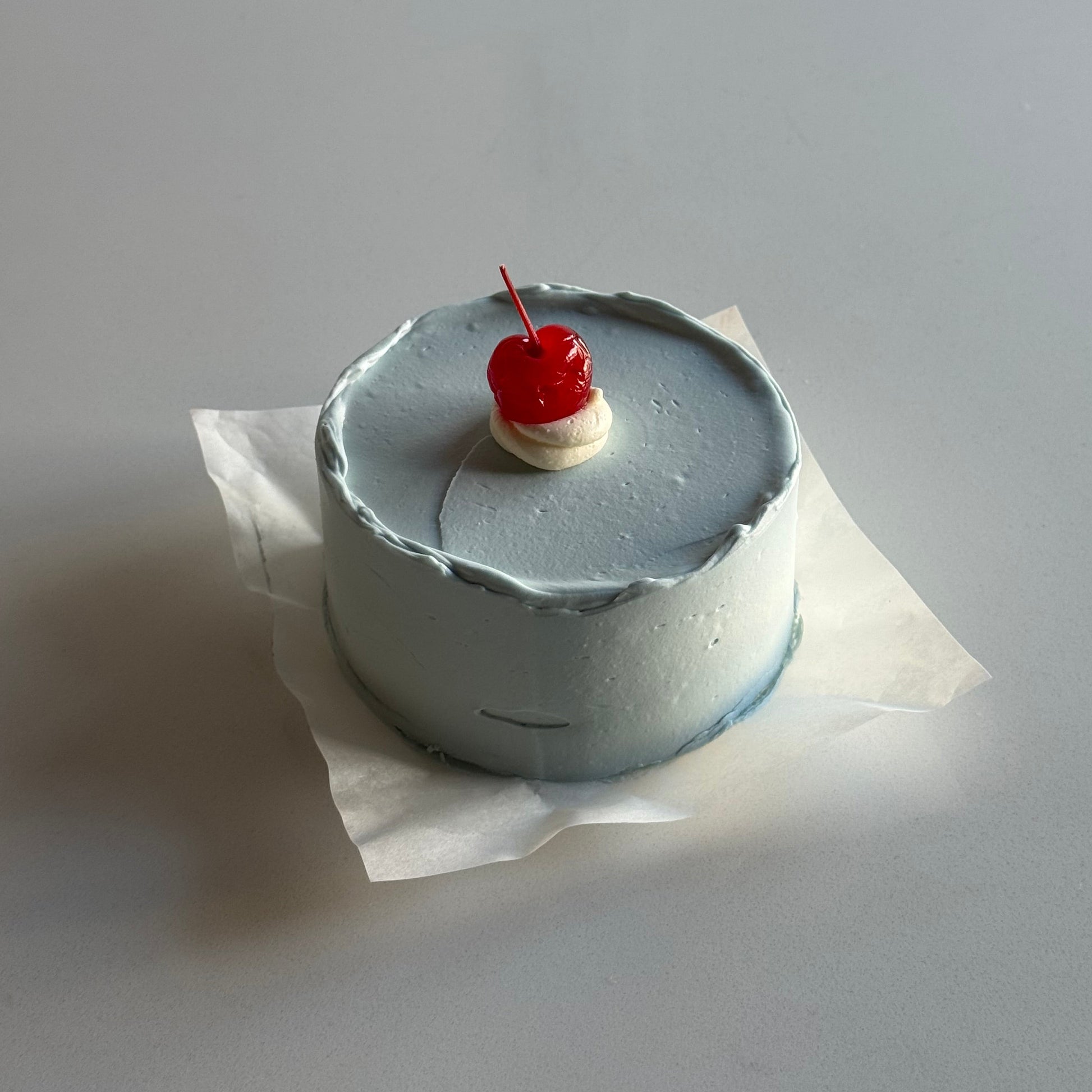 Small cake with a cherry on top against a plain background
