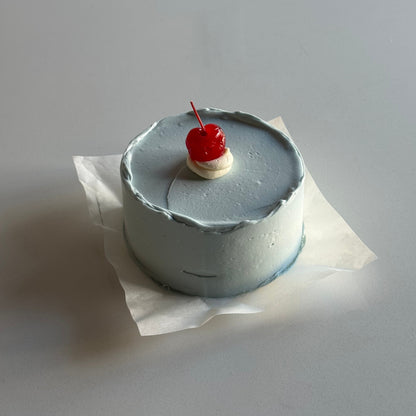 Small cake with a cherry on top against a plain background