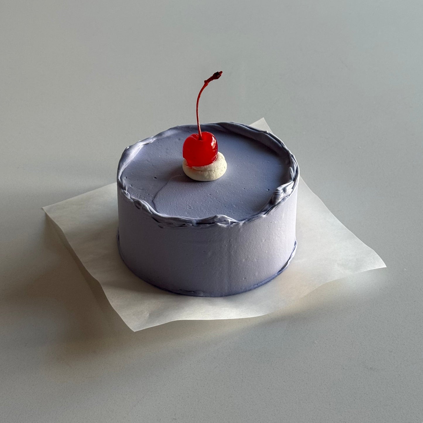 Small decorative item resembling a cake with a cherry on top, attached to a white surface.
