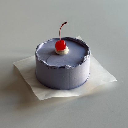 Small decorative item resembling a cake with a cherry on top, attached to a white surface.