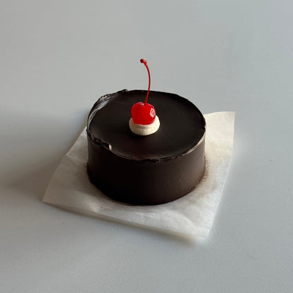 Small cake with a cherry on top on a white napkin against a light gray background
