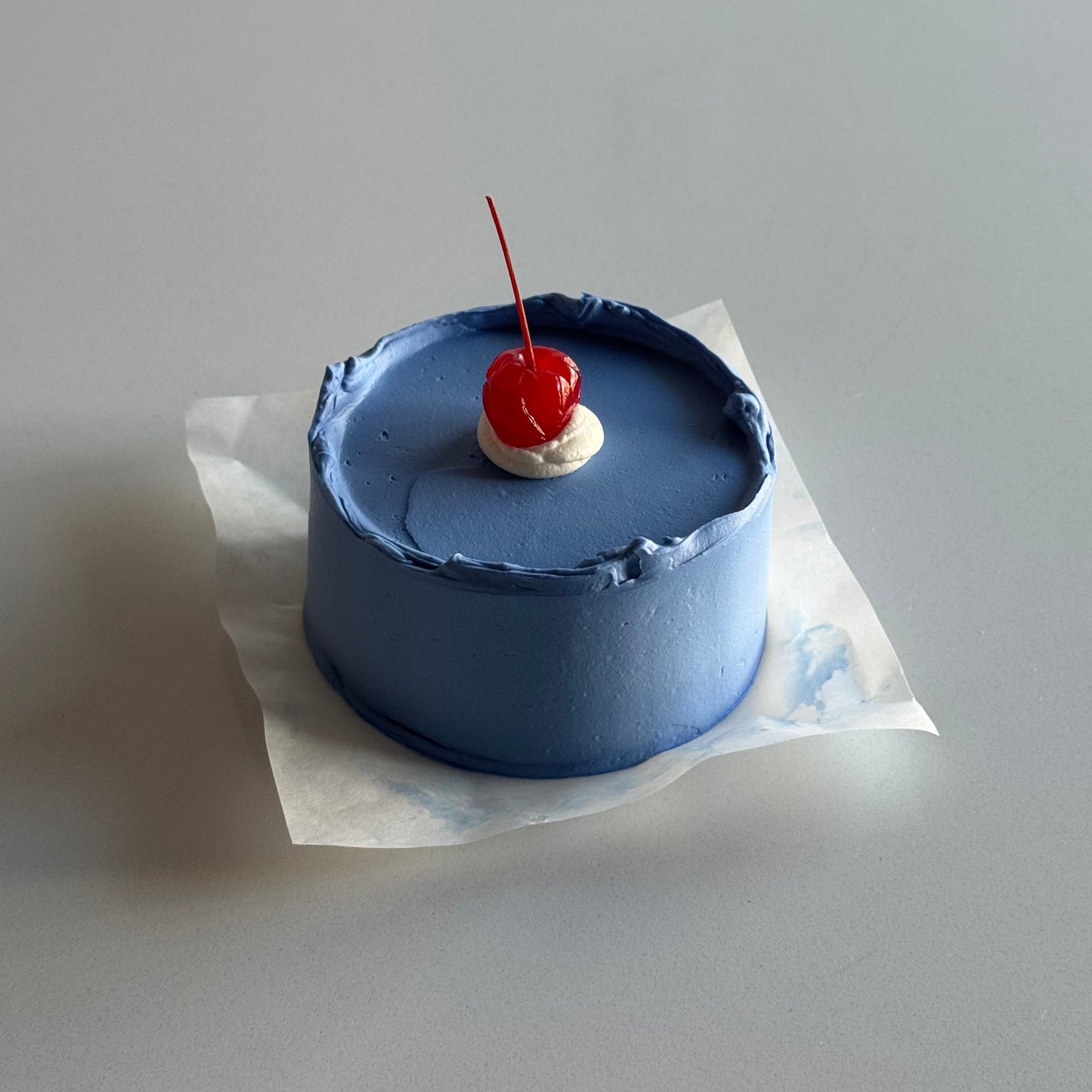 Small blue cake with a cherry on top against a plain background