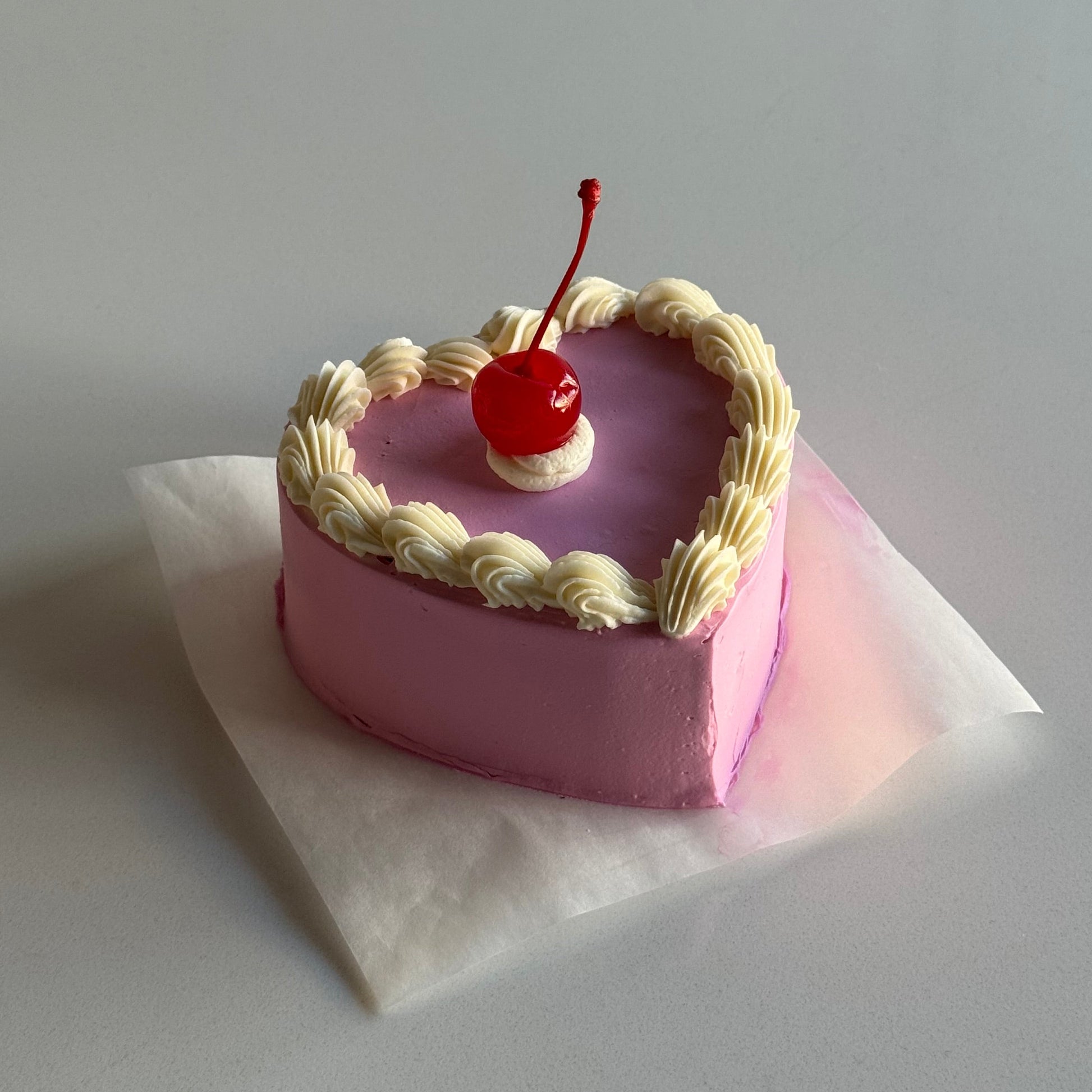 Pink decorative item with a cherry on top and white ribbon against a light gray background