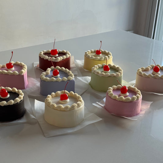 Assorted small cakes with cherries on top arranged on a white surface.